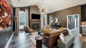 A modern living room with a fireplace, comfortable seating, a flat-screen TV, and a large window offering a view of the outdoors.