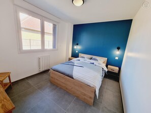 Une chambre à coucher avec un lit, une fenêtre, un radiateur et un luminaire fixé au mur.
