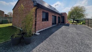 Un bâtiment en briques avec une allée en gravier, des plantes en pot et une cour clôturée.
