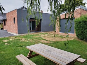 Une maison moderne avec une façade en briques, une couleur grise et une table de pique-nique en bois dans le jardin.