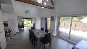 Une cuisine spacieuse équipée d’un réfrigérateur, un coin repas avec une grande table et des chaises, et une porte-fenêtre coulissante donnant sur un jardin.