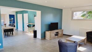 Un salon moderne avec un téléviseur, un coin repas et une cuisine en arrière-plan.