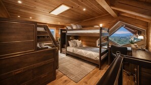Interior de una cabaña de madera con literas, un escritorio y vistas a través de un tragaluz.