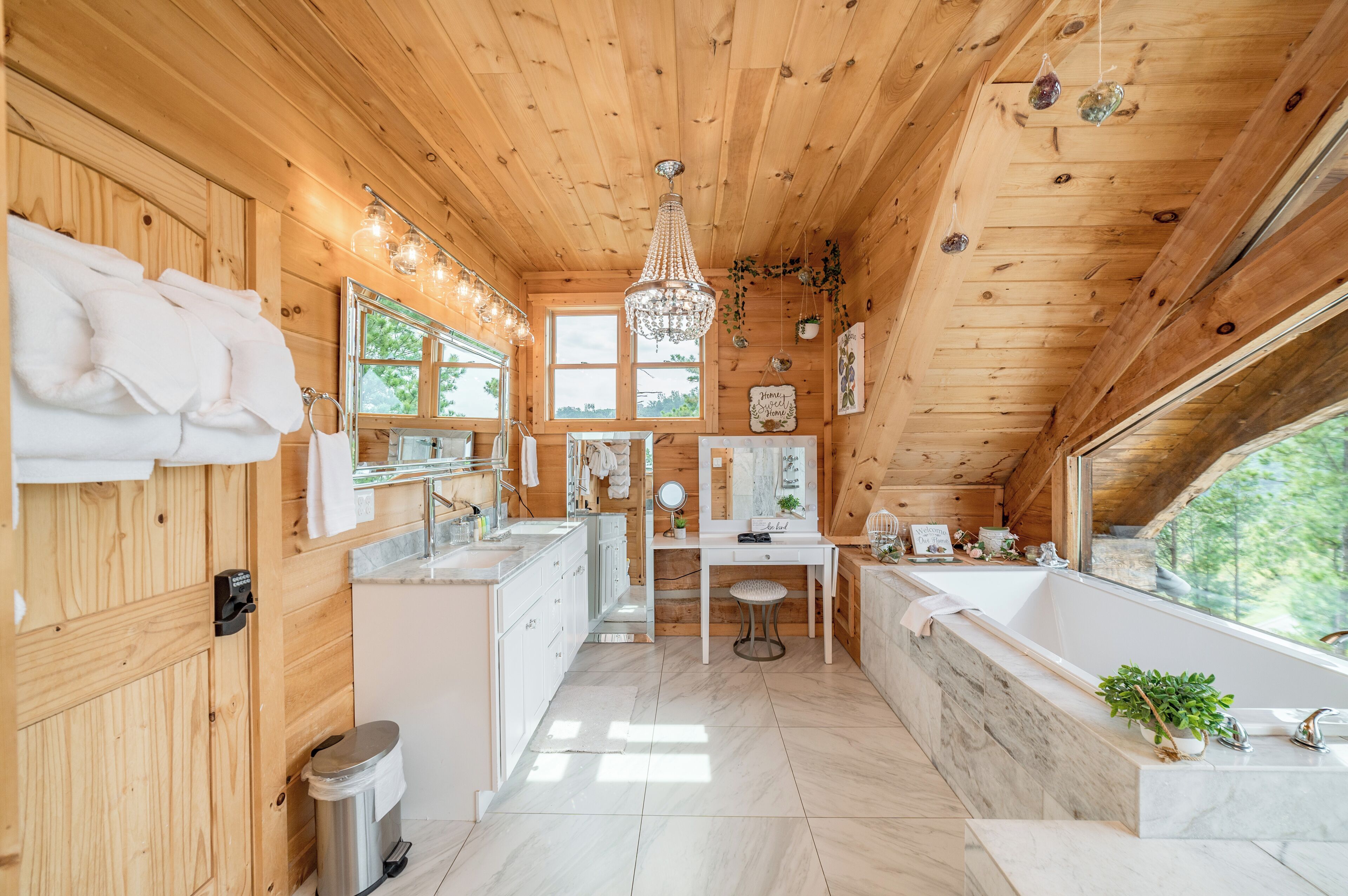 Interno di una baita in legno con bagno, mobiletto e una grande finestra.