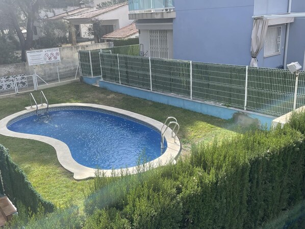 Une piscine entourée d’une clôture en métal, avec une pelouse bien entretenue et un bâtiment visible au loin.