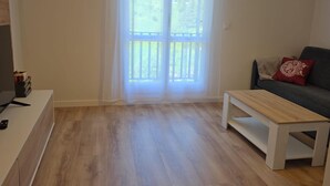 Un salon avec un plancher en bois, un canapé avec un coussin rouge, une table basse et un meuble pour la télévision.