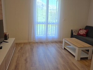 A living room with a wooden floor, a sofa with a red cushion, a coffee table, and a TV stand. - Modern studio near slopes - 4 guests (Aisa-Candanchú)