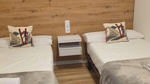 Une chambre d’hôtel avec deux lits, une tête de lit en bois, des tables de chevet et une petite table de nuit.