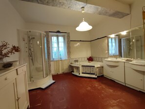 Ein Badezimmer mit Dusche, Waschbecken, Spiegel und einem Fenster mit gemusterten Vorhängen.