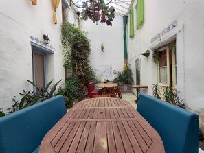 A courtyard with a wooden table and blue chairs, surrounded by white walls and greenery. - Spacious house by the Canal - 14 guests (Argeliers)