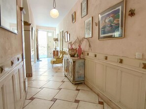A hallway with a tiled floor, a mirror, a lamp, a chair, a cabinet, and framed pictures on the wall. - Spacious house by the Canal - 14 guests (Argeliers)