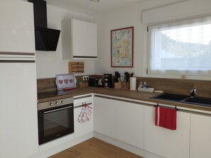 A modern kitchen with white cabinetry, a built-in oven, a coffee maker, and a window with a view of trees. - Cozy independent house - 2 guests (Saint-Étienne-lès-Remiremont)