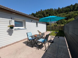 A patio with a table and chairs, a hanging flower pot, and a blue umbrella. - Cozy independent house - 2 guests (Saint-Étienne-lès-Remiremont)