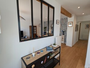 A modern living room with a large mirror, a console table with decorative items, a dining area with a wooden cabinet, and a hallway leading to another room. - Cozy independent house - 2 guests (Saint-Étienne-lès-Remiremont)