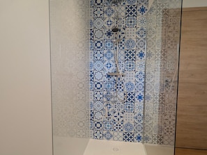 Un baño con azulejos estampados, zona de ducha y un mueble de madera.