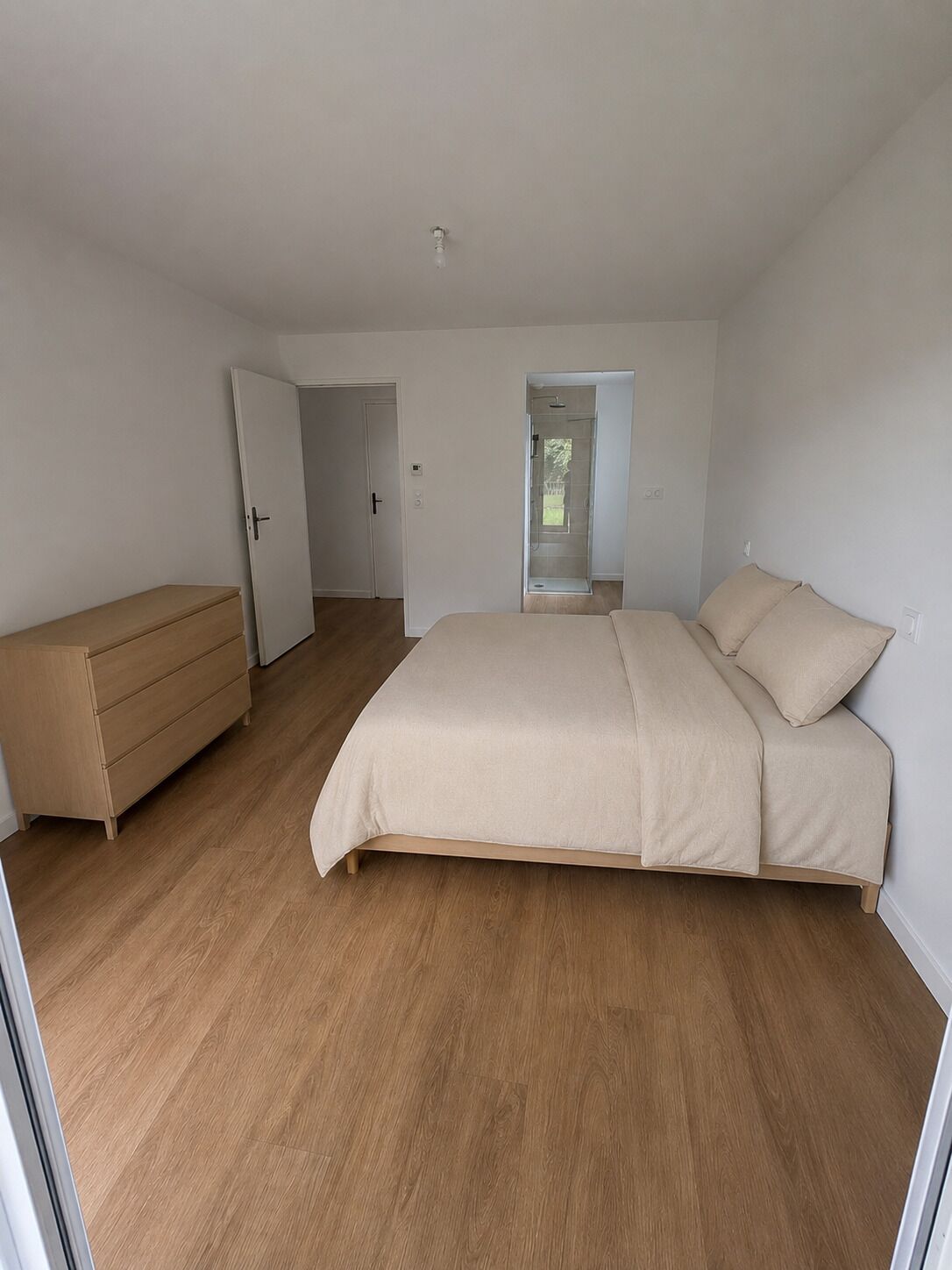A bedroom with a bed, a dresser, and a door leading to another room.