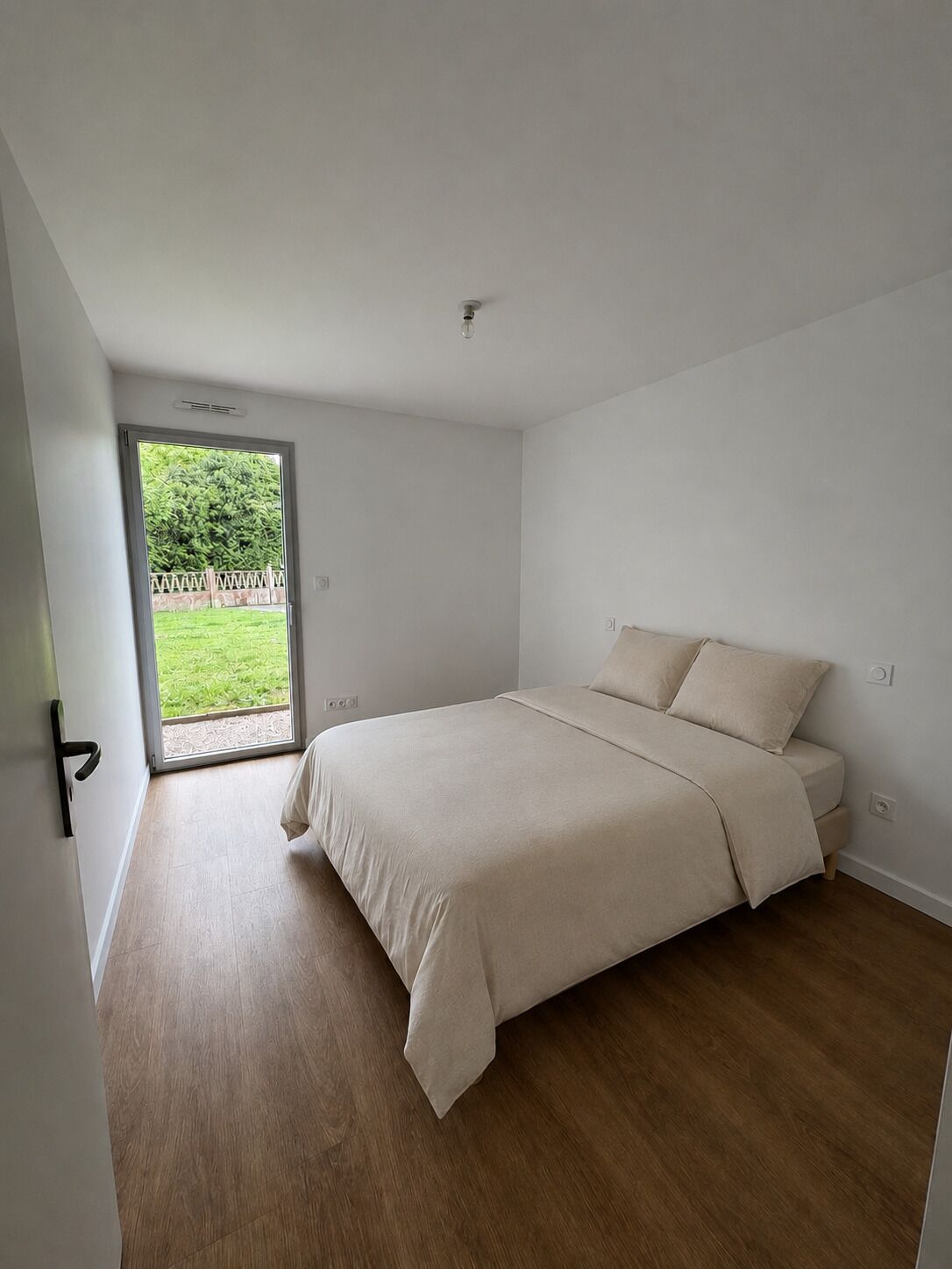 Une chambre à coucher avec un lit, une porte donnant sur un balcon et un interrupteur sur le mur.