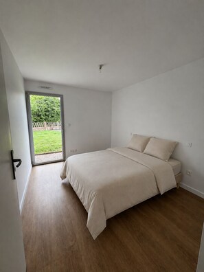 Ein Schlafzimmer mit einem Bett, einer Tür, die auf einen Balkon führt, und einem Lichtschalter an der Wand.