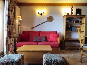 A cozy living room with a red sofa, wooden coffee table, and a unique wall-mounted paddle. - Charming apartment mountain view - 6 guests (Les Arcs 1800)