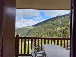A wooden deck with a table and chairs, overlooking a forested mountain range. - Charming apartment mountain view - 6 guests (Les Arcs 1800)
