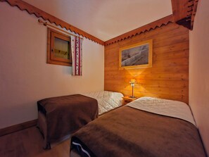 A room with two beds, wooden walls, a window with curtains, a painting, and a nightstand with a lamp. - Charming apartment mountain view - 6 guests (Les Arcs 1800)