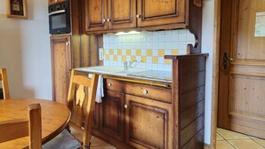 Een keuken met houten kastjes, een betegelde spatwand, een spoelbak en een fornuis.