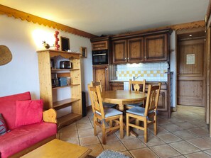 Eine kompakte Küche mit Holzausbau, einem Esstisch mit Stühlen, einem roten Sofa und einer kleinen Holzregaleinrichtung.