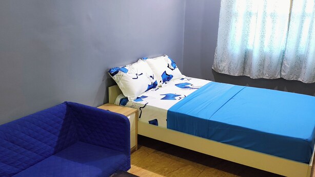 A room with a bed, a blue sofa, a small table, and a window with a curtain. - Room-budget Studio Room In Lome Togo (Lomé)