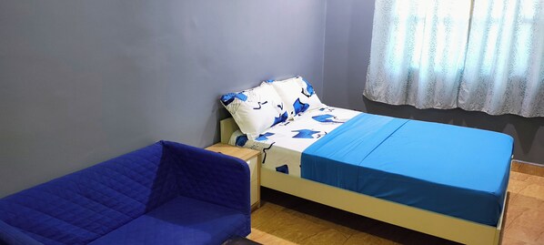 Ein Zimmer mit einem Bett, einem blauen Sofa, einem kleinen Tisch und einem Fenster mit Vorhang.