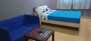 Ein Zimmer mit einem blauen Sofa, einem Bett mit blauer Bettdecke und einem kleinen Tisch mit einer Fernbedienung.