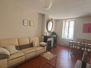 A living room with a sofa, a small table, a fireplace, and a dining area with chairs. - Cozy apartment in city center - 2 guests (Narbonne)