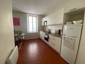 A compact kitchen with white cabinets, a built-in oven, a refrigerator, and a window with natural light. - Cozy apartment in city center - 2 guests (Narbonne)