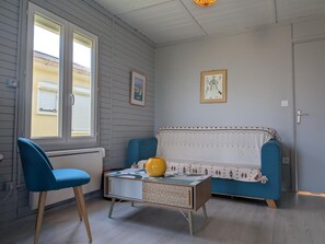 Ein Zimmer mit einem blauen Sofa, einem blauen Sessel, einem kleinen Tisch mit einer gelben Vase und einer gemusterten Decke auf dem Sofa.