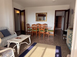 Ein Wohnzimmer mit einer Couch, einem Esstisch mit Stühlen, einem Spiegel und einer kleinen Küchenzeile.