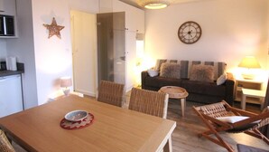 Een eethoek met een houten tafel, rieten stoelen, een kleine ronde tafel met een lamp, een bank met kussens, een wandklok en een ster decoratie.