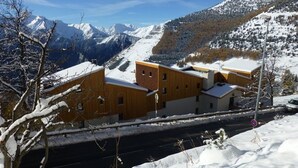 Een modern gebouw met een plat dak en een opvallende ingang, omgeven door met sneeuw bedekte bergen en een heldere lucht.