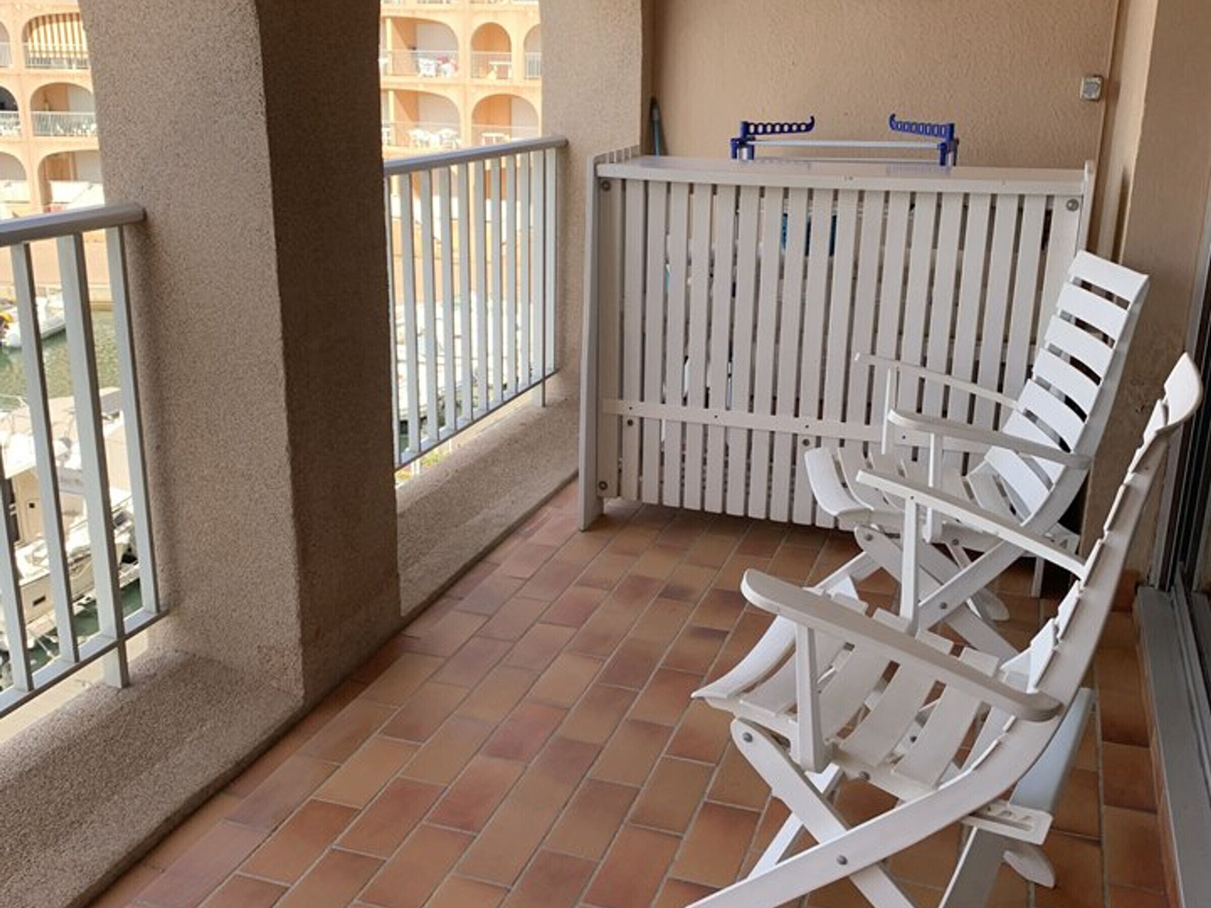 A balcony with white chairs, a white railing, and a view of a building with multiple balconies.