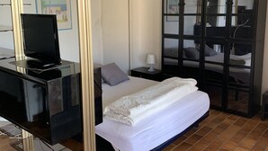Hotellihuone, jossa on sänky, työpöytä, jossa on televisio, yöpöytä ja vaatekaappi.