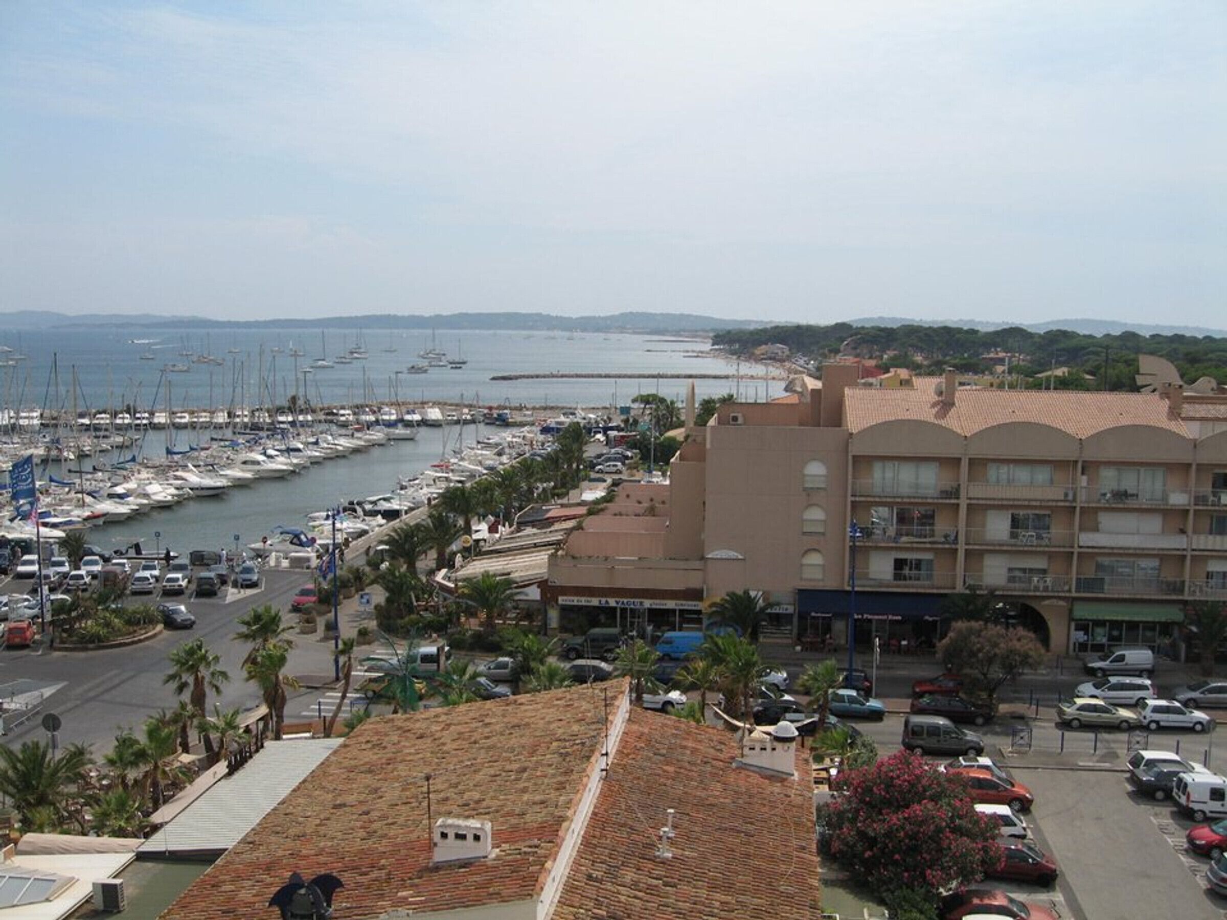 Uma marina costeira com barcos, um estacionamento e um edifício com varandas viradas para a água.