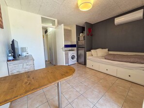 Ein kleines Zimmer mit Bett, Waschmaschine und einer Kochnische.
