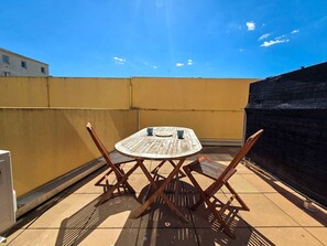Eine kleine Terrasse im Freien mit einem runden Holztisch und zwei Holzstühlen.