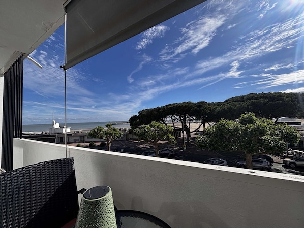 Un balcon avec vue sur la mer, les arbres et les voitures garées.