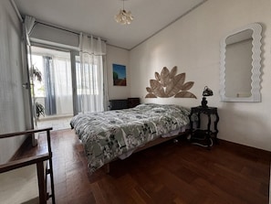 Une chambre à coucher avec un lit, un radiateur, un miroir et une fenêtre avec des rideaux.