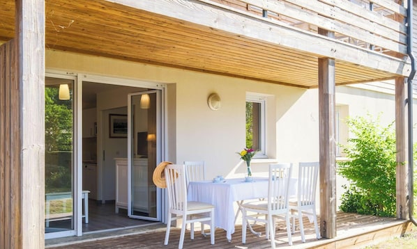 Ein überdachter Essbereich im Freien mit Tisch und Stühlen, ein Glastür-Eingang und eine Holzterrasse.