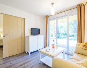 Ein Zimmer mit Holztür, einem weißen Schrank mit Fernseher, einem Tisch mit einer Zeitschrift und einer Couch mit einem Hut.