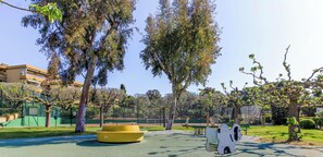 Ein Park mit Spielgeräten, Bäumen und einem Tennisplatz.