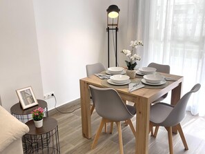 A dining area with a wooden table, grey chairs, white plates, a black floor lamp, and a potted plant. - Beachside Apartment with AC, 2 Bedrooms, Terrace & Garden Views (La Pineda)