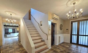 A staircase leading to a second floor, a chandelier, and a large window with blinds.