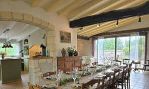 A dining area with stone walls, wooden beams, and a long table set for a meal.