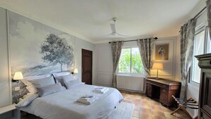 A bedroom with a bed, a desk, a radiator, a window with curtains, a ceiling fan, and a wall painting. - House with pool, pets allowed - 12 guests (Monsaguel)